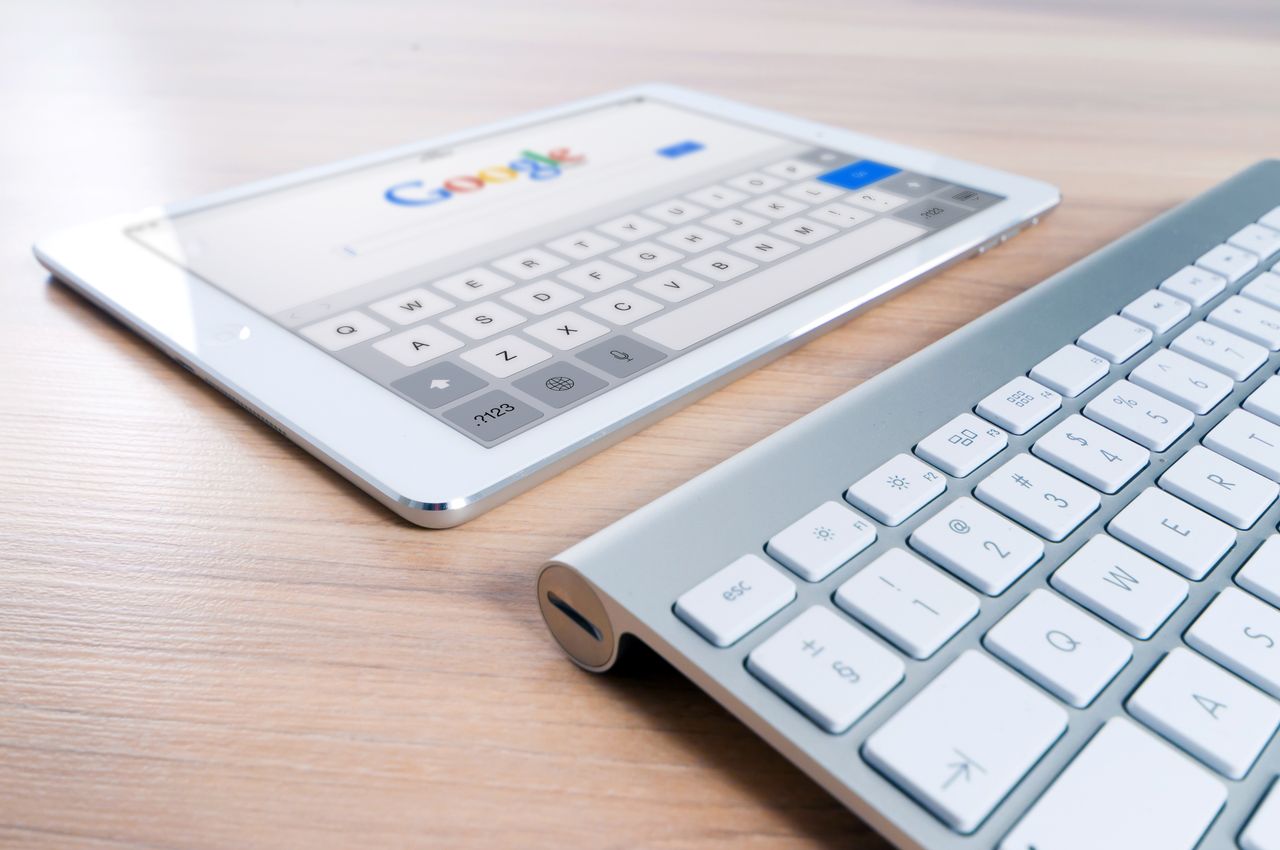 Une tablette moderne affichant le logo d’un moteur de recherche, posée à côté d’un clavier sans fil sur un bureau en bois.